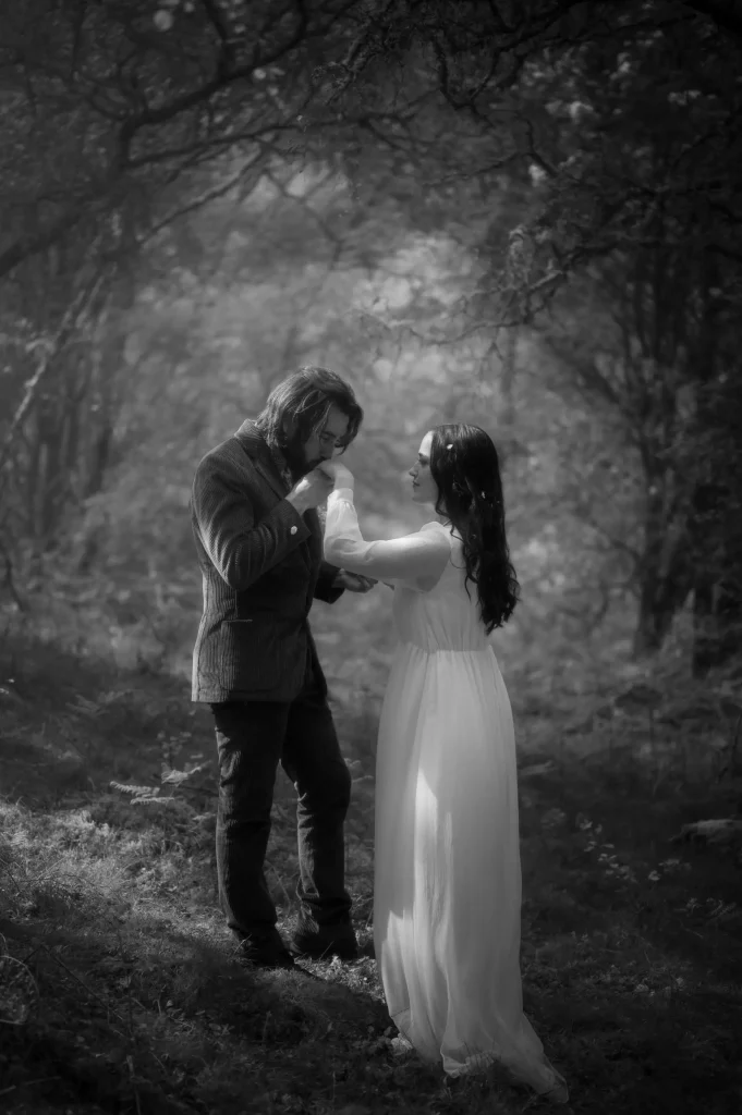 a groom kissing bride's hand under trees
